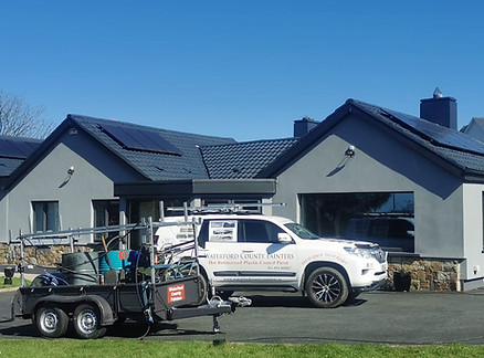 House with solar panels, a trailer, and white SUV parked outside.